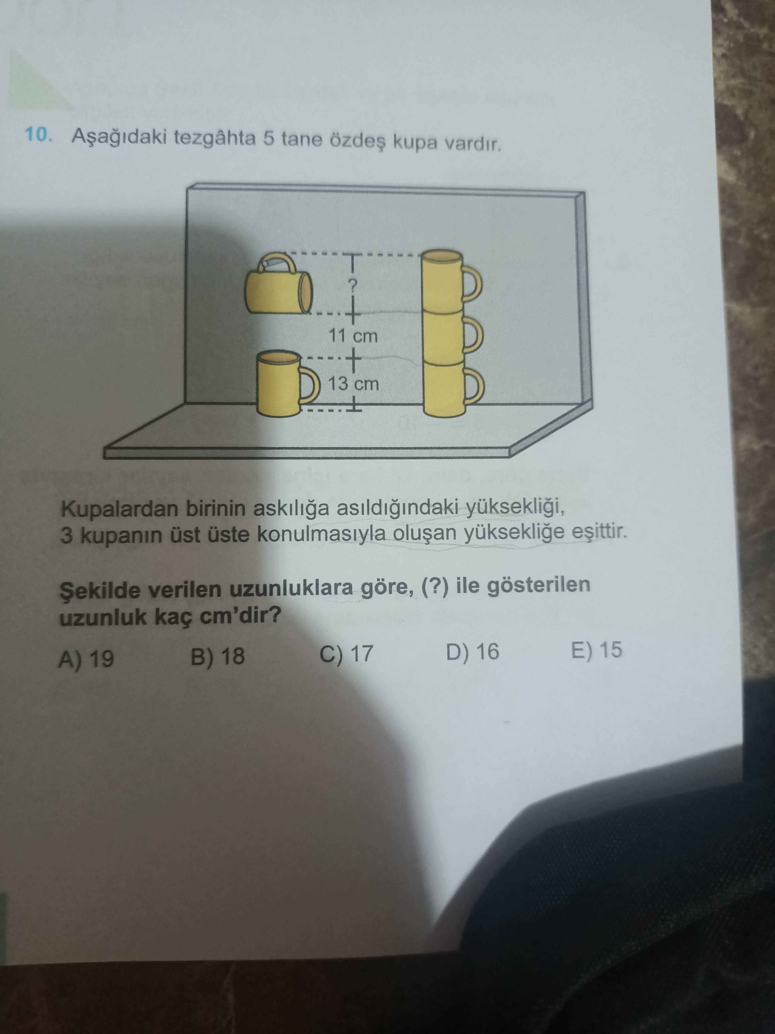 Aşağıdaki tezgâhta 5 tane özdeş kupa vardır. Kupalardan birinin askılığa asıldığındaki yüksekliği, 3
